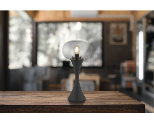 Stolní lampa s průhledným skleněným stínidlem a žárovkou na dřevěném stole