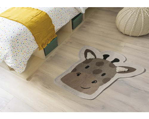 Pokojová scéna s postelí, sedákem a kobercem ve tvaru hlavy žirafy.