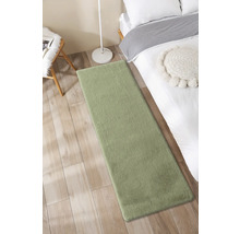 Zelený koberec vedle postele na dřevěné podlaze