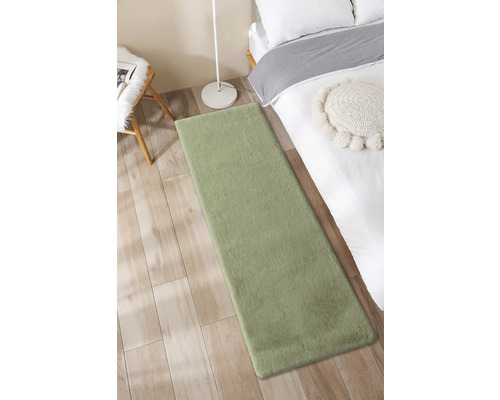 Zelený koberec vedle postele na dřevěné podlaze