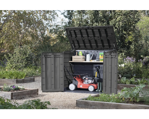 Zahradní skříň s otevřeným víkem a dveřmi na zahradě, s sekačkou na trávu a zahradním nářadím