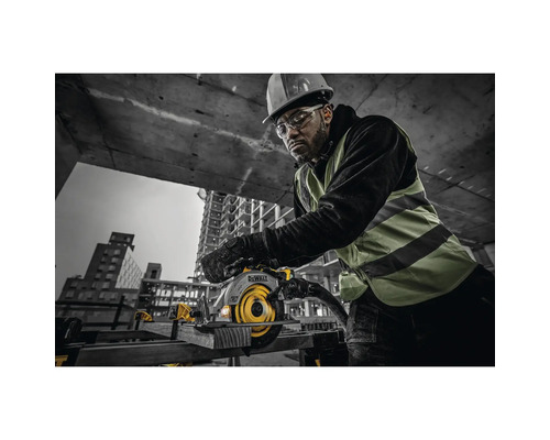 Muž s ochrannou helmou a brýlemi obsluhuje ruční kotoučovou pilu značky DeWalt na staveništi