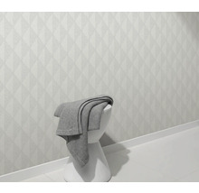 Světlá stěna s geometrickým vzorem a stolička s dekou