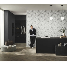 Pohled na pokoj s tapetou se vzorem, komodou, osvětlením a mužem