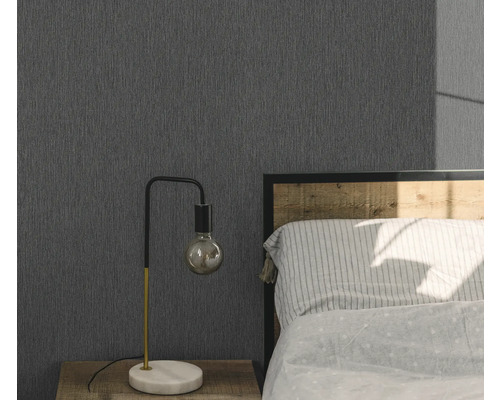 Ložnice s šedou strukturovanou tapetou, nočním stolkem a lampou.