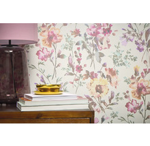 Detailní pohled na stěnu s květinovou tapetou, doplněnou lampou, knihami a miskou na dřevěném nábytku.