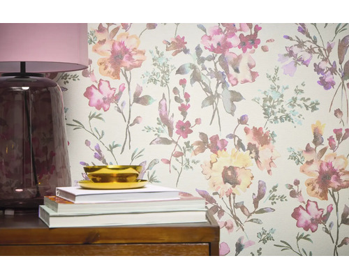 Detailní pohled na stěnu s květinovou tapetou, doplněnou lampou, knihami a miskou na dřevěném nábytku.