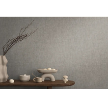 Dekorativní zátiší s vázou, mísou a okrasnými předměty na dřevěném stole před šedou zdí.