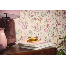 Interiérová scéna s květinovou tapetou, stolní lampou, vázami, knihami a miskou.