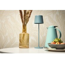 Dekorativní zátiší se stolní lampou, vázou a termoskou na pozadí vzorované tapety.