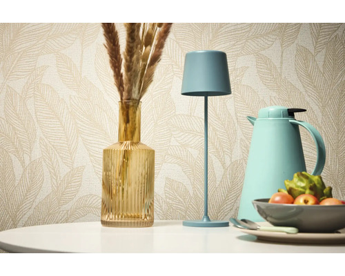 Dekorativní zátiší se stolní lampou, vázou a termoskou na pozadí vzorované tapety.