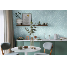 Světlá místnost se stolem, židlemi a kuchyňským koutem před stěnou s tapetou s listovým motivem.