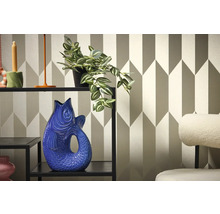 Dekorativní interiér s policí, rostlinou a vázou ve tvaru ryby na pozadí geometrické tapety.