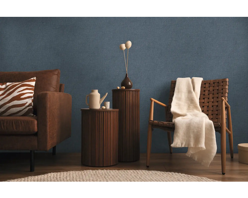 Obývací pokoj s pohovkou, křeslem, příručními stolky a dekoracemi na modré strukturované tapetě