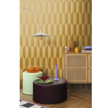 Ukázka vybavení interiéru s lampou, různými stolky a skříňkou před tapetou s geometrickým vzorem.