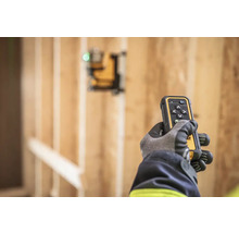 Ruka v rukavici drží dálkové ovládání laseru DeWalt před dřevěnou konstrukcí.