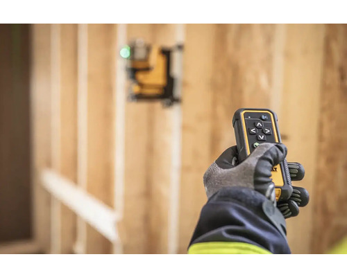 Ruka v rukavici drží dálkové ovládání laseru DeWalt před dřevěnou konstrukcí.