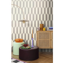 Interiér s geometrickou tapetou, stojací lampou, komodou a dekorativními předměty.