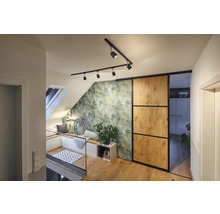 Světlá podkrovní byt s střešním oknem, posezením, zelenou tapetou s motivem listů, posuvnými dveřmi a dřevěnou podlahou.