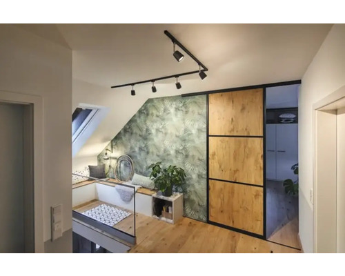 Světlá podkrovní byt s střešním oknem, posezením, zelenou tapetou s motivem listů, posuvnými dveřmi a dřevěnou podlahou.