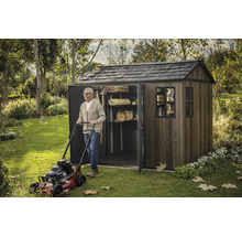 Muž se sekačkou na trávu před zahradní kůlnou s policemi