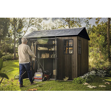 Muž tlačí sekačku do zahradní skříně s policemi pro uložení zahradního nářadí