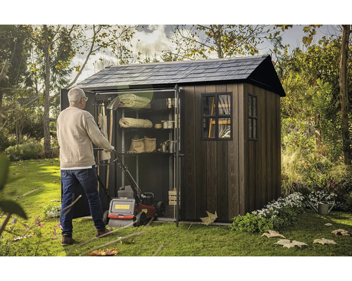 Muž tlačí sekačku do zahradní skříně s policemi pro uložení zahradního nářadí