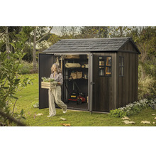 Zahradní scéna s kůlnou na nářadí, sekačkou na trávu a ženou nesoucí truhlík s květinami.