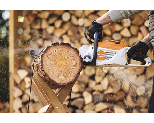 Osoba řeže kus dřeva motorovou pilou Stihl na kozové pile.