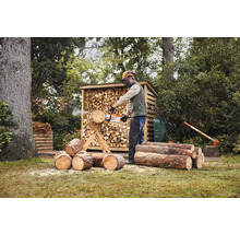 Muž řeže dřevo motorovou pilou před kůlnou na dřevo na zahradě.