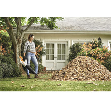 Žena používá foukač listí na zahradě před domem s hromadou listí