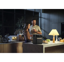 Pár v kuchyni s přenosným generátorem energie, který napájí lampu, zatímco v pozadí běží mikrovlnná trouba.