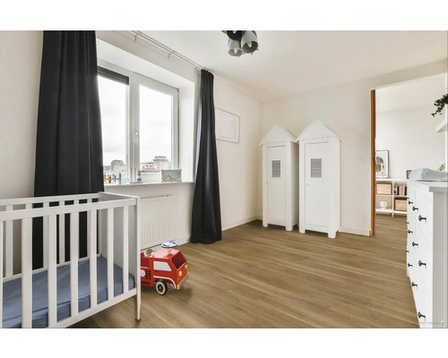 Světlý dětský pokoj s dětskou postýlkou, hračkou hasičského auta a dvěma skříněmi ve tvaru domu.