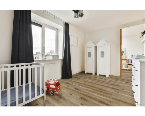 Světly dětský pokoj s dětskou postýlkou, dřevěnou podlahou a bílým nábytkem.