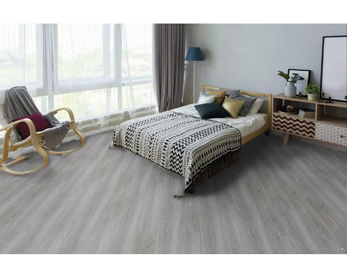 Světlá ložnice s dřevěnou postelí, vzorovanou denní dekou, dřevěným houpacím křeslem a komodou na podlaze