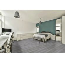 Světlý, uspořádaný pokoj s postelí, stolem a šedou dřevěnou podlahou