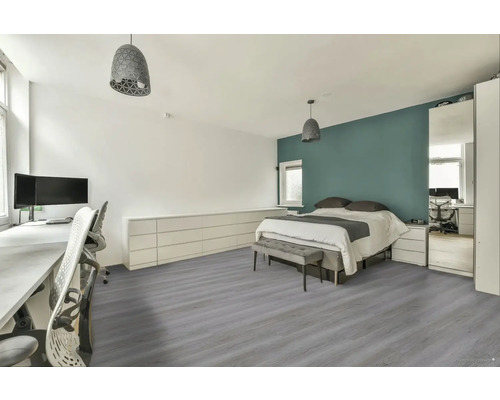 Světlý, uspořádaný pokoj s postelí, stolem a šedou dřevěnou podlahou