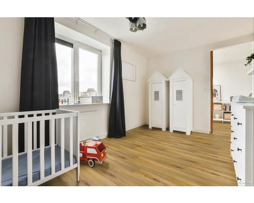 Světlý dětský pokoj s dětskou postýlkou, dřevěnou podlahou a dvěma bílými skříněmi ve stylu plážového domu.