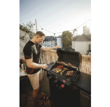 Muž griluje zeleninu a maso na plynovém grilu na balkóně.