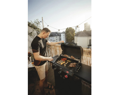 Muž griluje zeleninu a maso na plynovém grilu na balkóně.