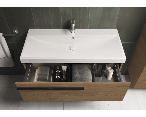 Skříňka pod umyvadlo s otevřenou zásuvkou, vybavená ručníky a koupelnovými potřebami.