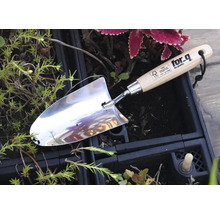 Nerezová jamkovač s dřevěnou rukojetí v zahradním záhonu