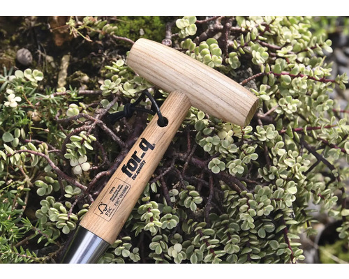 Zahradní nářadí s dřevěnou rukojetí a logem for-q, obklopené rostlinami