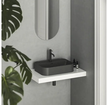 Moderní koupelna s černým umyvadlem na desku, baterií a oválným zrcadlem nad bílou policí.