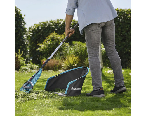 Zahradní scéna se zahradníkem zametajícím trávník hráběmi na listí a sběračem trávy od firmy Gardena