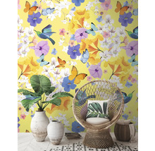 Dekorativní interiér se žlutou tapetou, zdobenou květinami, motýly a ptáky, doplněný o proutěné křeslo a pokojové rostliny