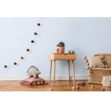 Světlý dětský pokoj s dřevěnou podlahou, dřevěným stolem, ratanovým křeslem a dekorativními prvky, jako je girlanda, polštáře a rostlina.