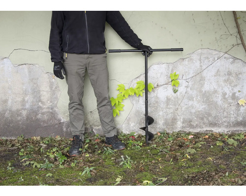 Osoba se zemním vrtákem na zahradě