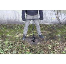 Osoba používá zemní vrták k vyvrtání díry do země.