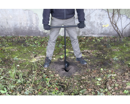 Osoba používá zemní vrták k vyvrtání díry do země.